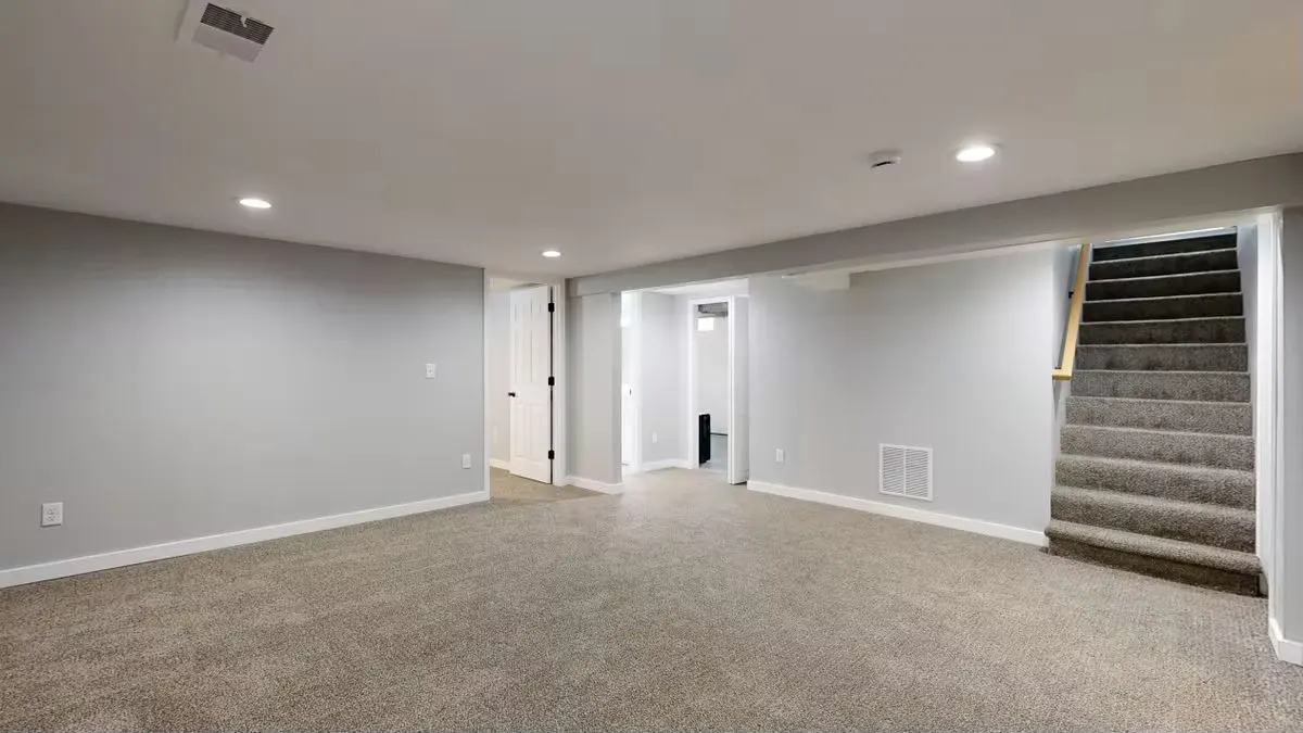 Empty modern basement with beige carpet and white walls, ideal for renovation.